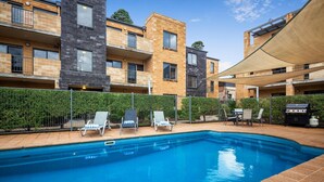 Un moderno complejo de apartamentos con piscina, mobiliario de exterior y zona de barbacoa.