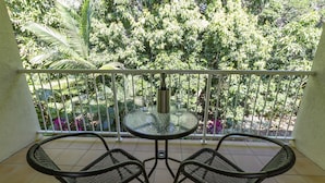 Varanda com mesa de vidro redonda e duas cadeiras de vime, delimitada por um corrimão branco.