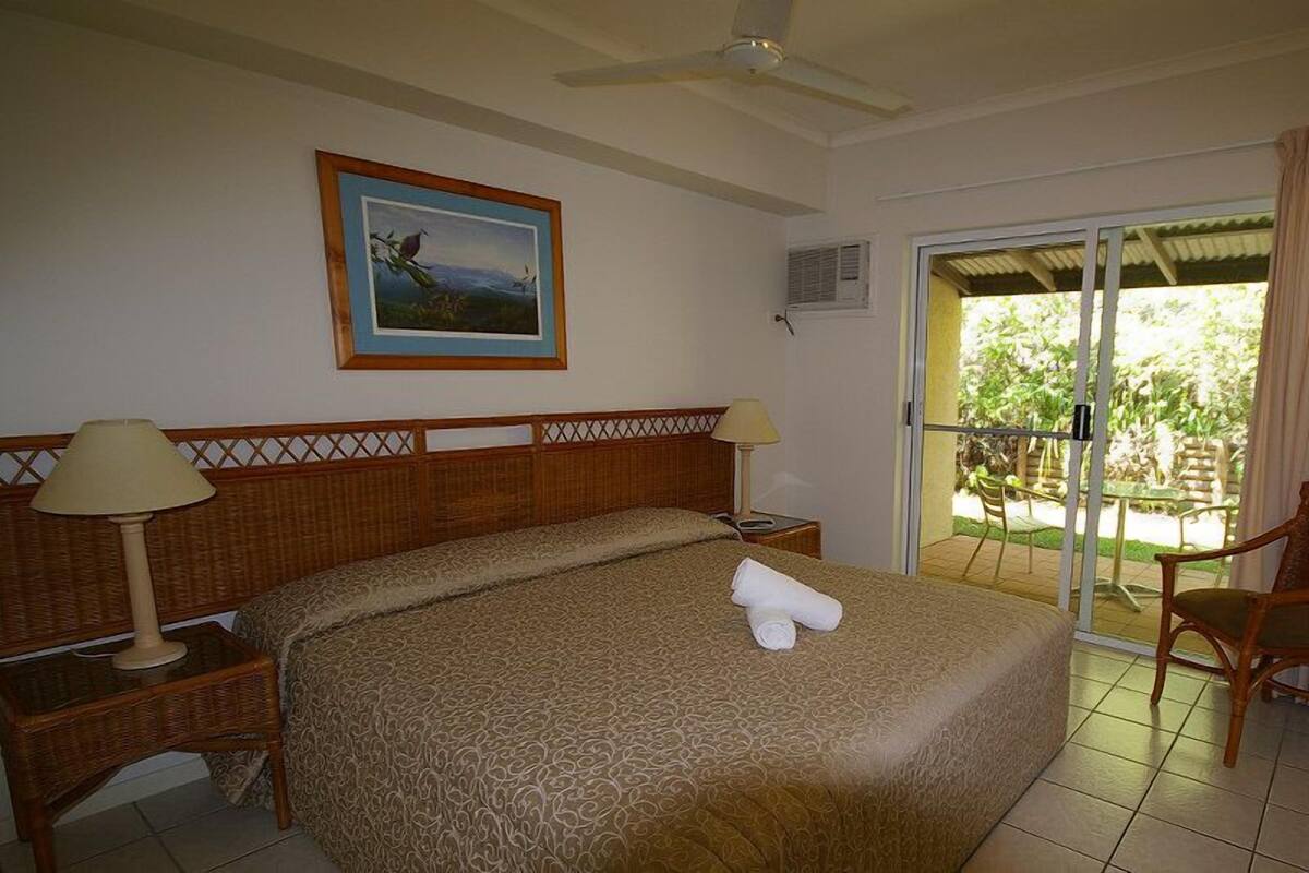 A hotel room with a bed, two bedside lamps, a painting on the wall, and a view of the outdoors through a sliding glass door.