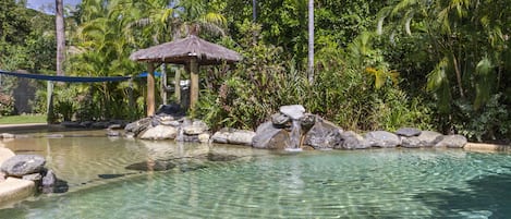 Una piscina al aire libre, una piscina con cascada, tumbonas