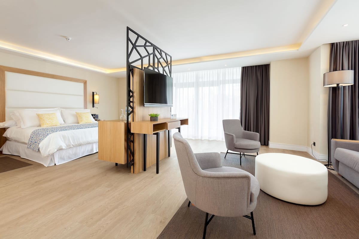 Ein modernes Hotelzimmer mit Bett, Schreibtisch, Fernseher, Sessel und einer Couch.