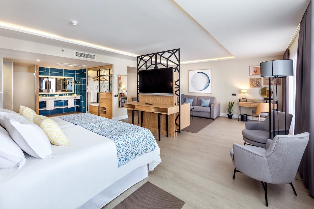 Ein modernes Hotelzimmer mit einem großen Bett, einem Schreibtisch, einem Fernseher und einer Sitzecke.