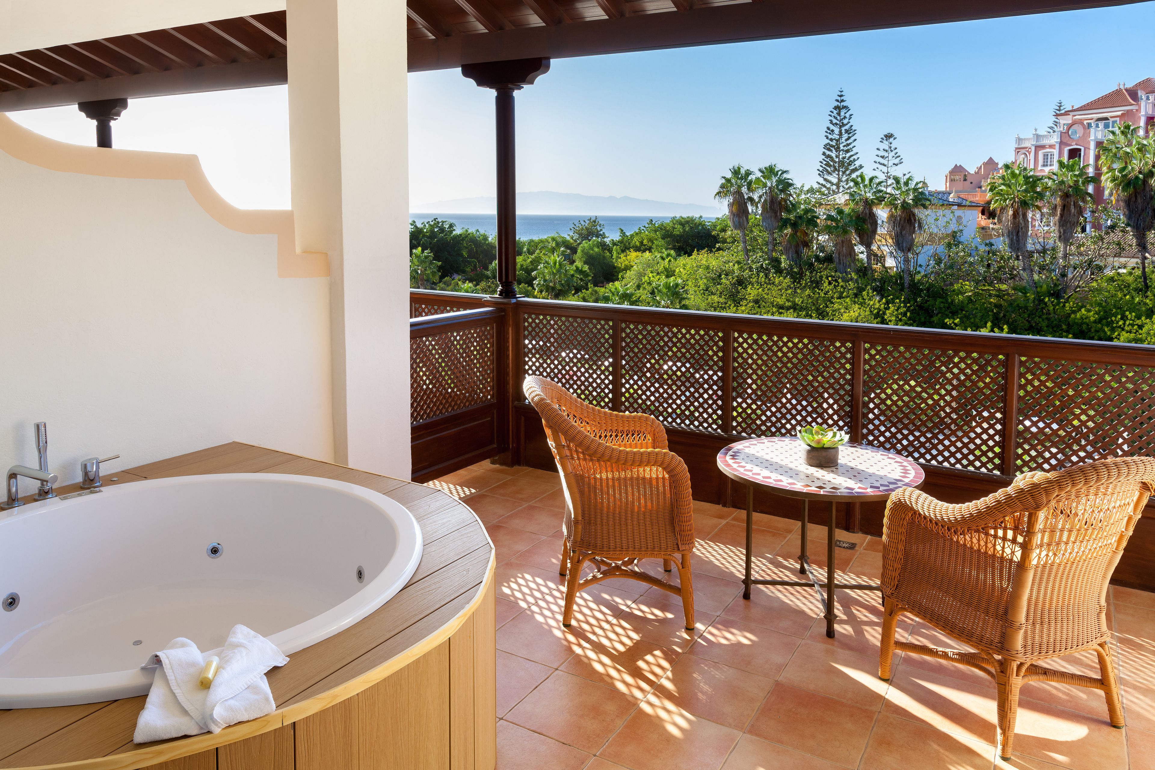 A balcony with a bathtub, wicker chairs, and a table with a plant.