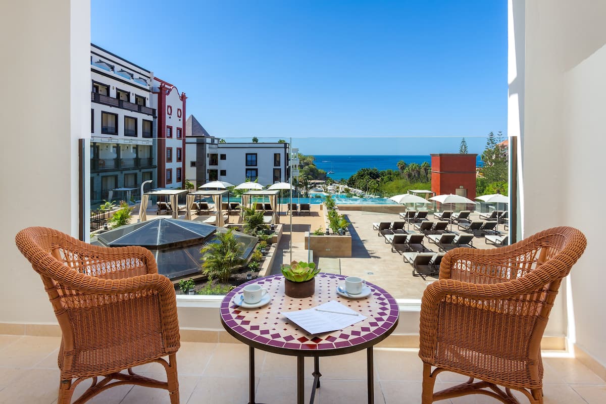 Ein Balkon mit Korbstühlen, einem Tisch mit einer Pflanze und Blick auf einen Pool und Gebäude.