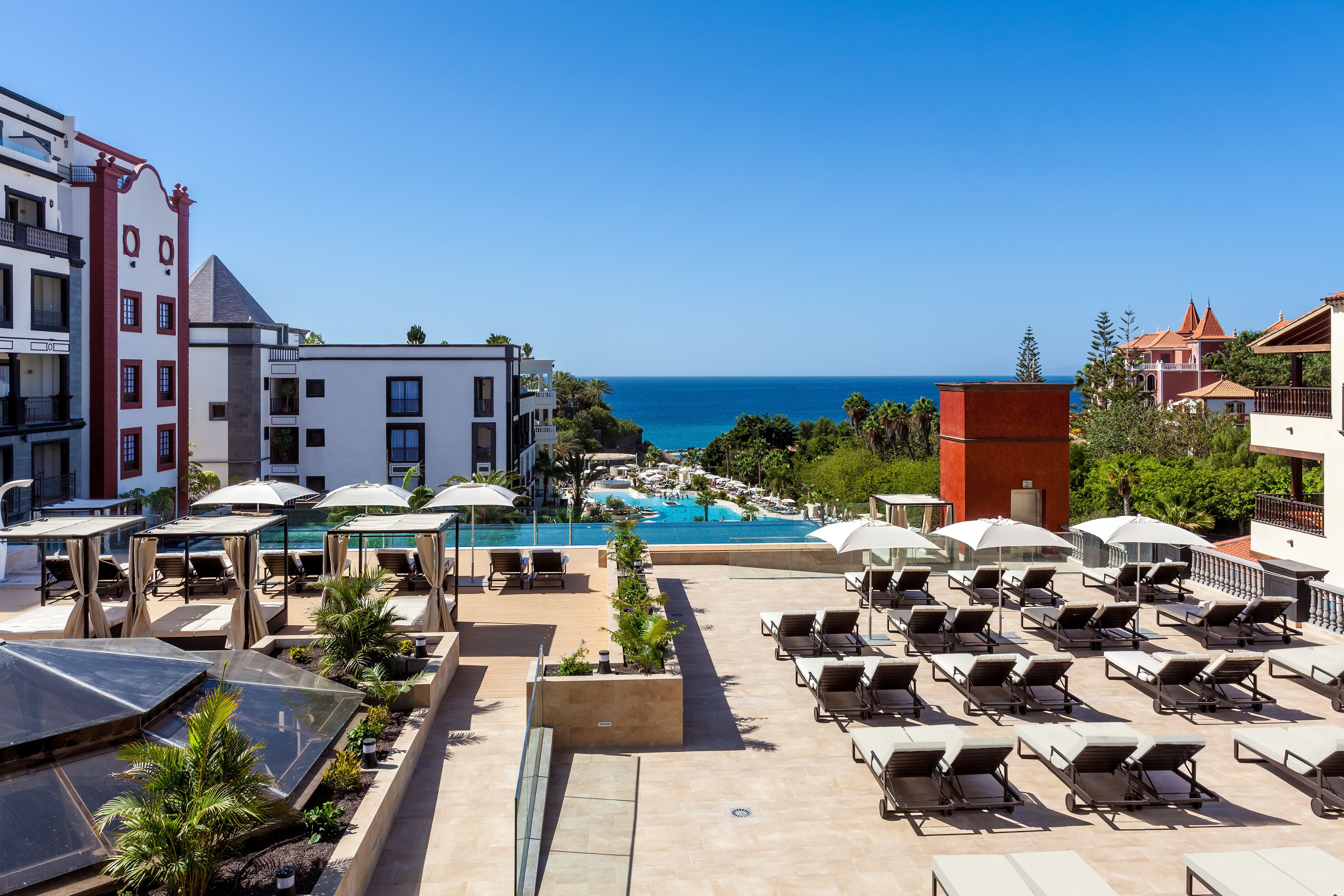 A rooftop pool area with sun loungers and umbrellas, overlooking a clear blue sea.
