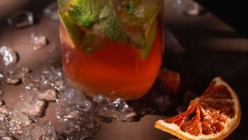 Un verre avec une paille noire, décoré de feuilles de menthe et d’une tranche d’orange sanguine, entouré de glaçons.
