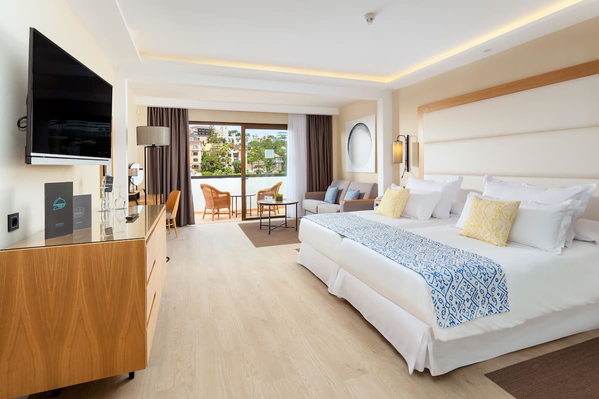 Ein modernes Hotelzimmer mit einem großen Bett, einem Schreibtisch, einem Fernseher und einem Balkon mit Blick auf die Stadt.