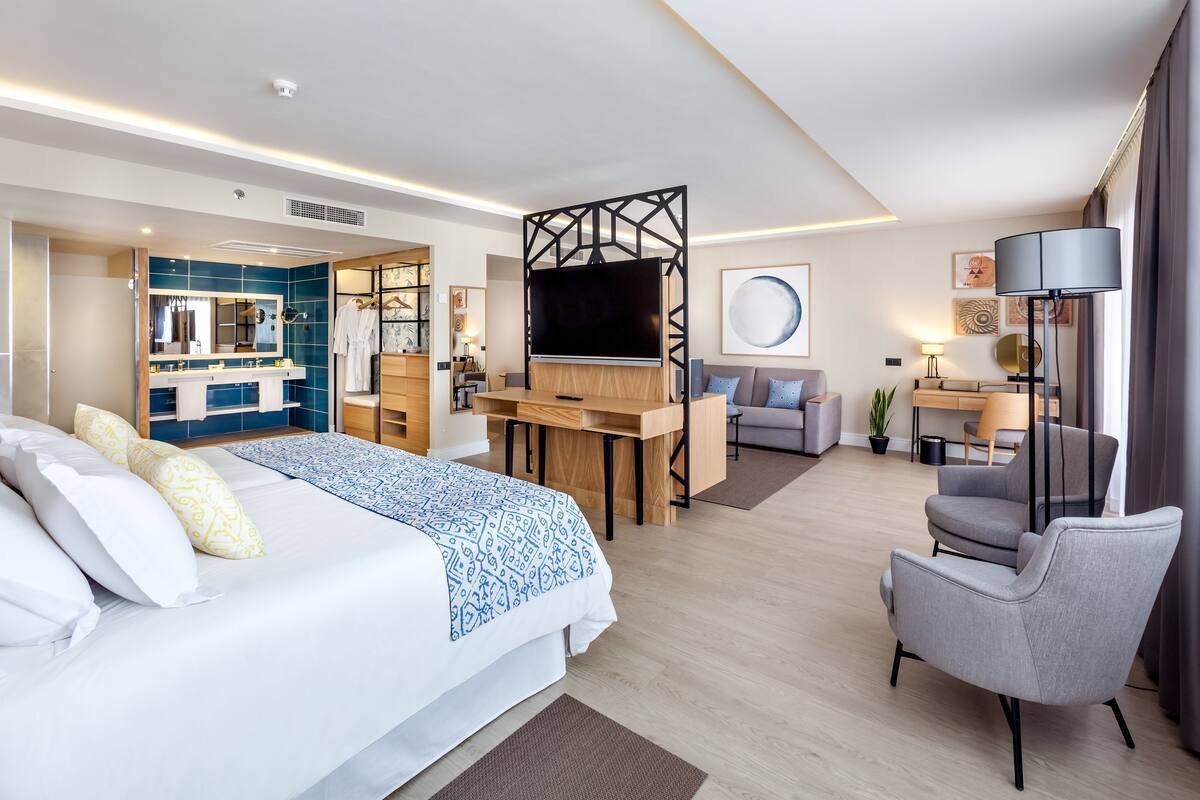 Ein modernes Hotelzimmer mit einem großen Bett, einem Schreibtisch, einem Fernseher und einer Sitzecke.
