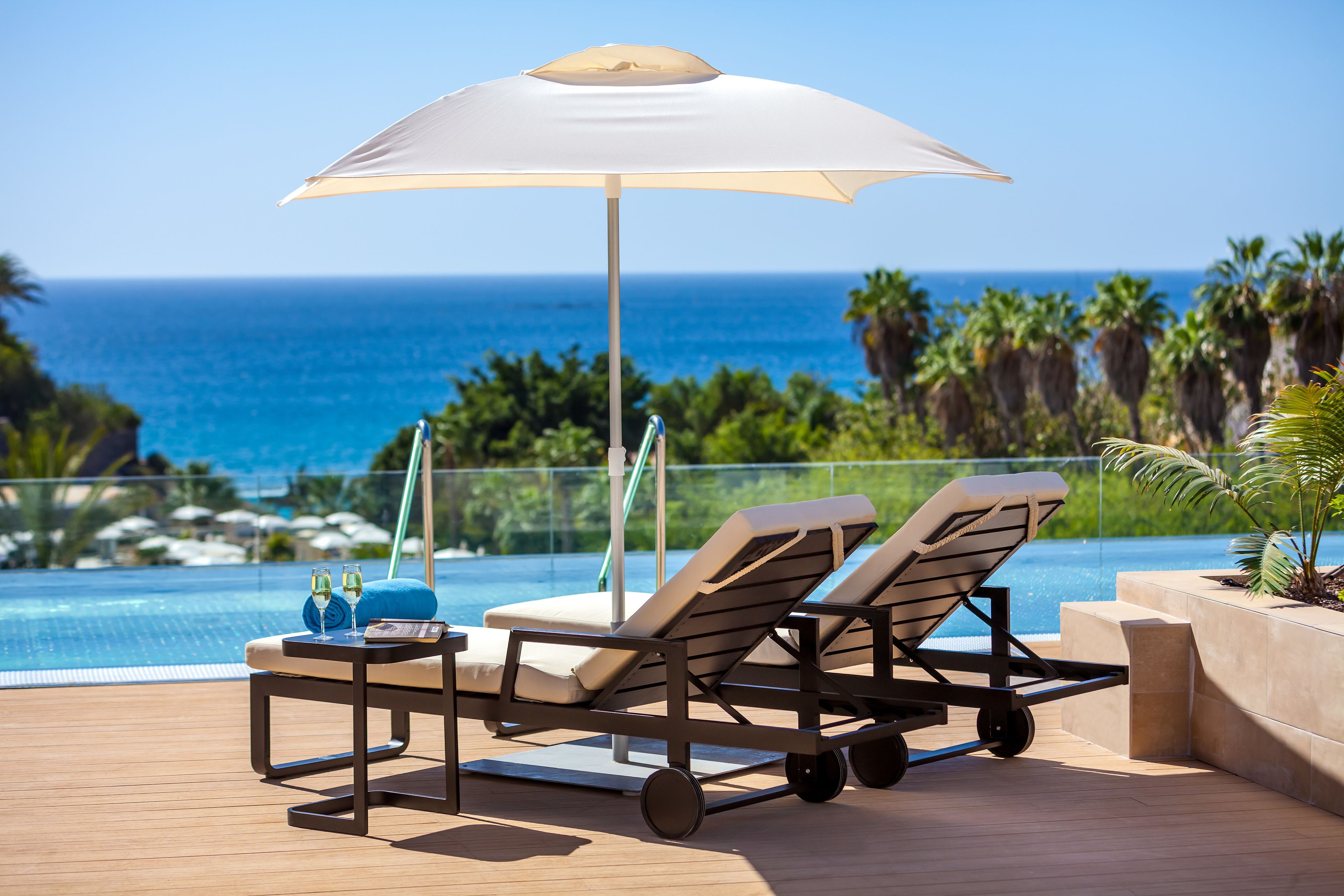 Un espace aménagé au bord de la piscine, avec deux chaises longues, une table avec des boissons et un grand parasol.