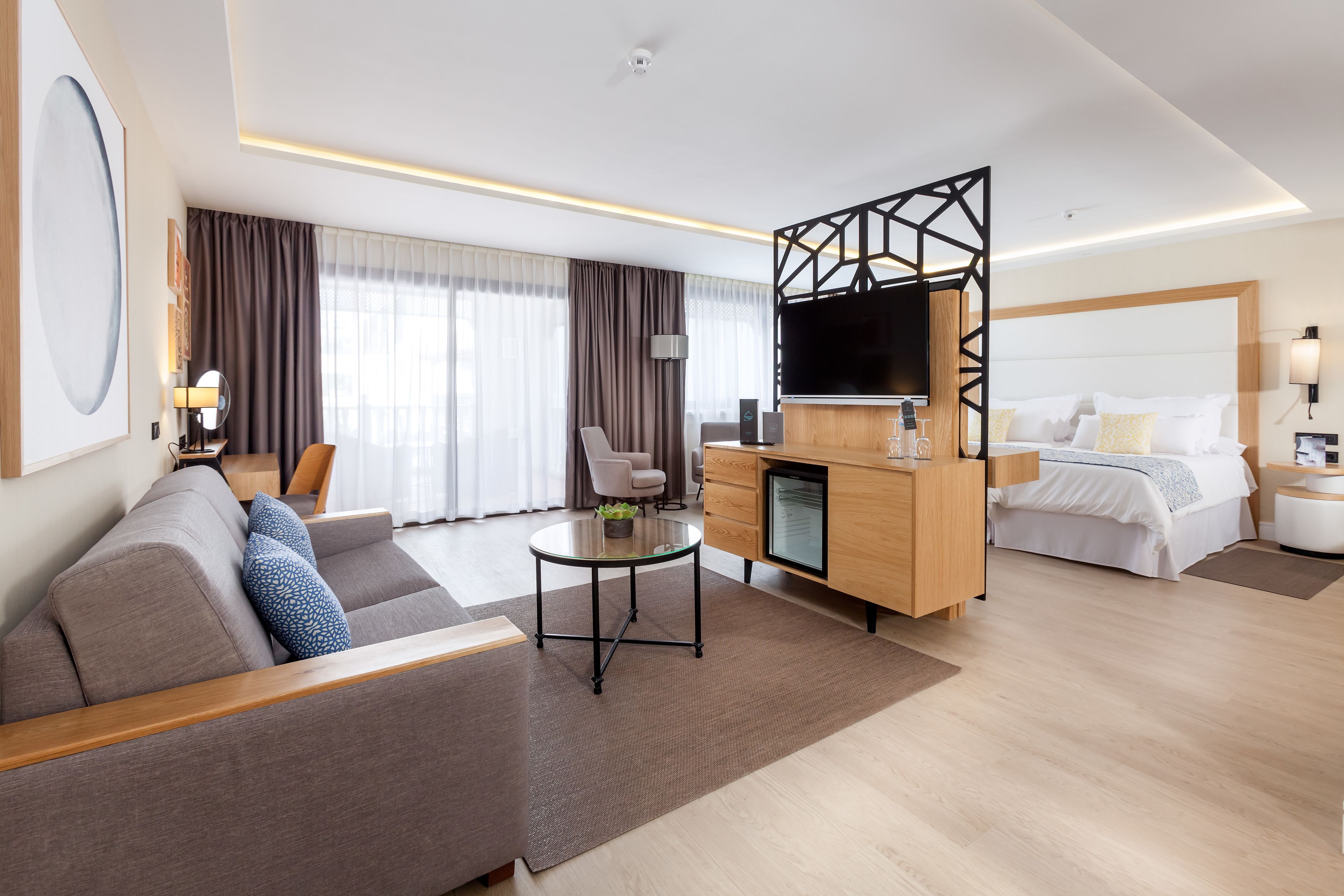 A modern hotel room with a sofa, a dining table, a TV, a bed, and a desk.