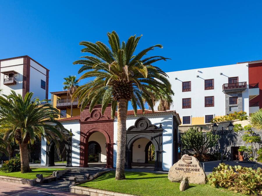 Edificio histórico con un arco central, palmeras y un cartel que dice "CENPLAGE GRAN TACANDE".