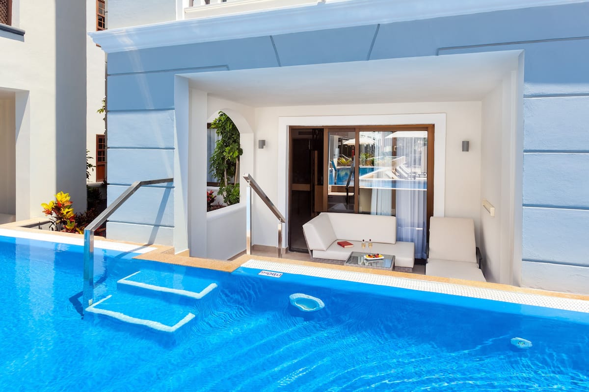 Ein moderner Hotelpoolbereich mit Pool, einer kleinen Sitzecke inklusive Sofa und Tisch sowie einer Treppe zu den oberen Etagen.