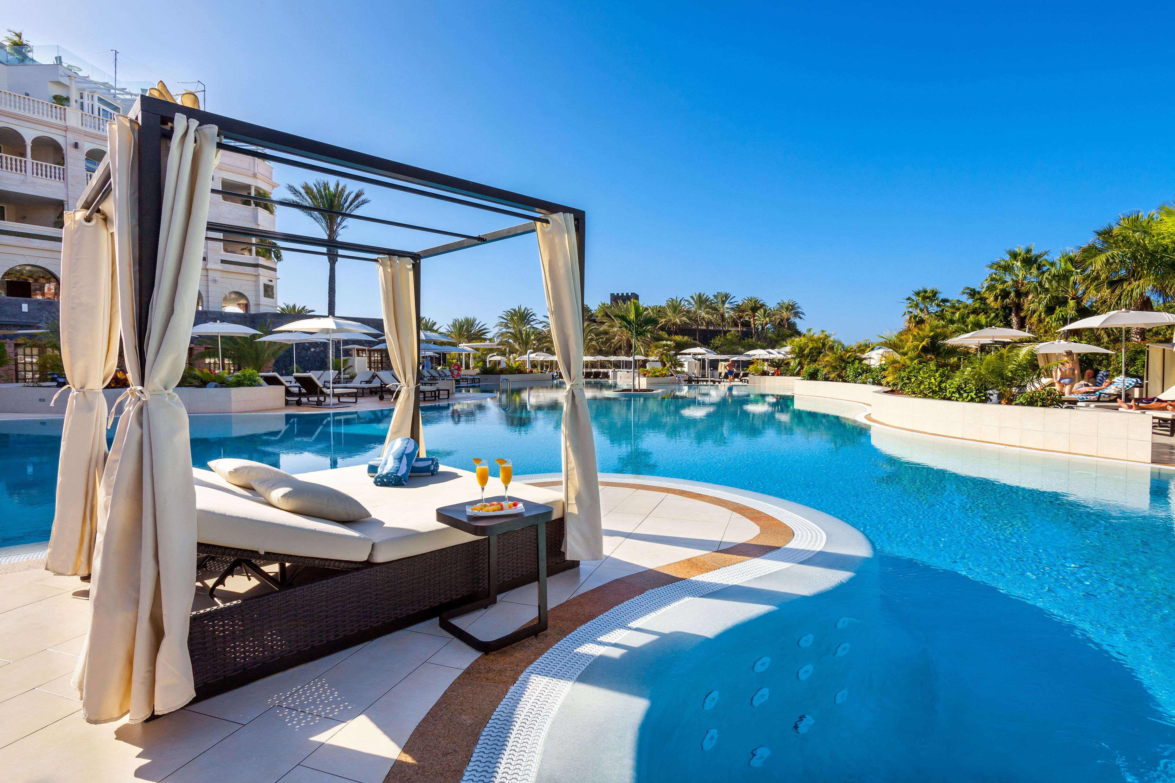 Una zona de piscina amb gandules, una cabana i ombrelles.