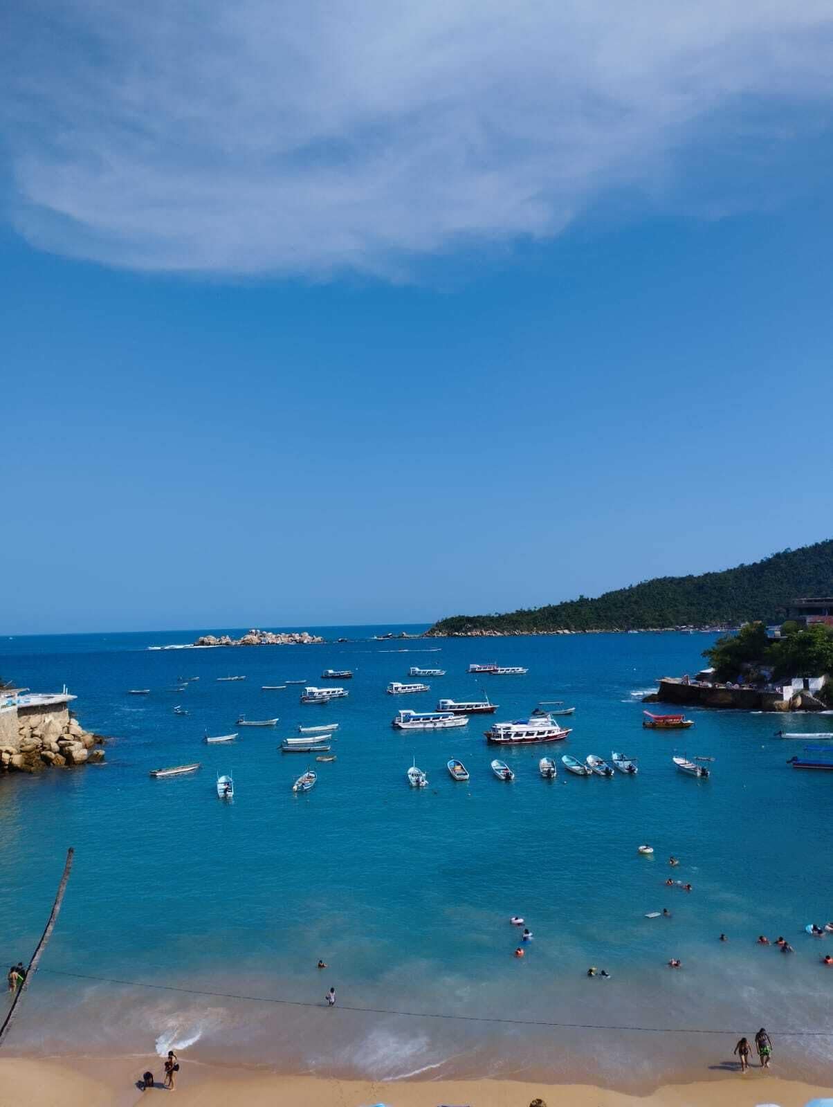 Vista costera con barcos, una playa de arena y terreno rocoso.