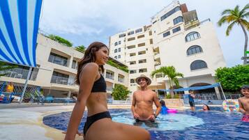 Relax by the pool surrounded by palm trees and a multi-story building with balconies.