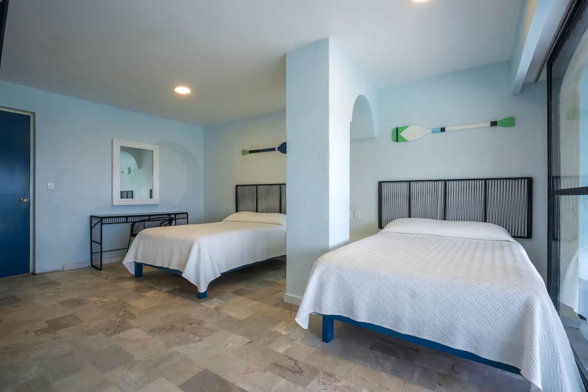 A room with two beds, a desk, and a large window.