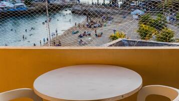Un balcón con una mesa redonda y dos sillas, con vista a un puerto lleno de barcos y gente.