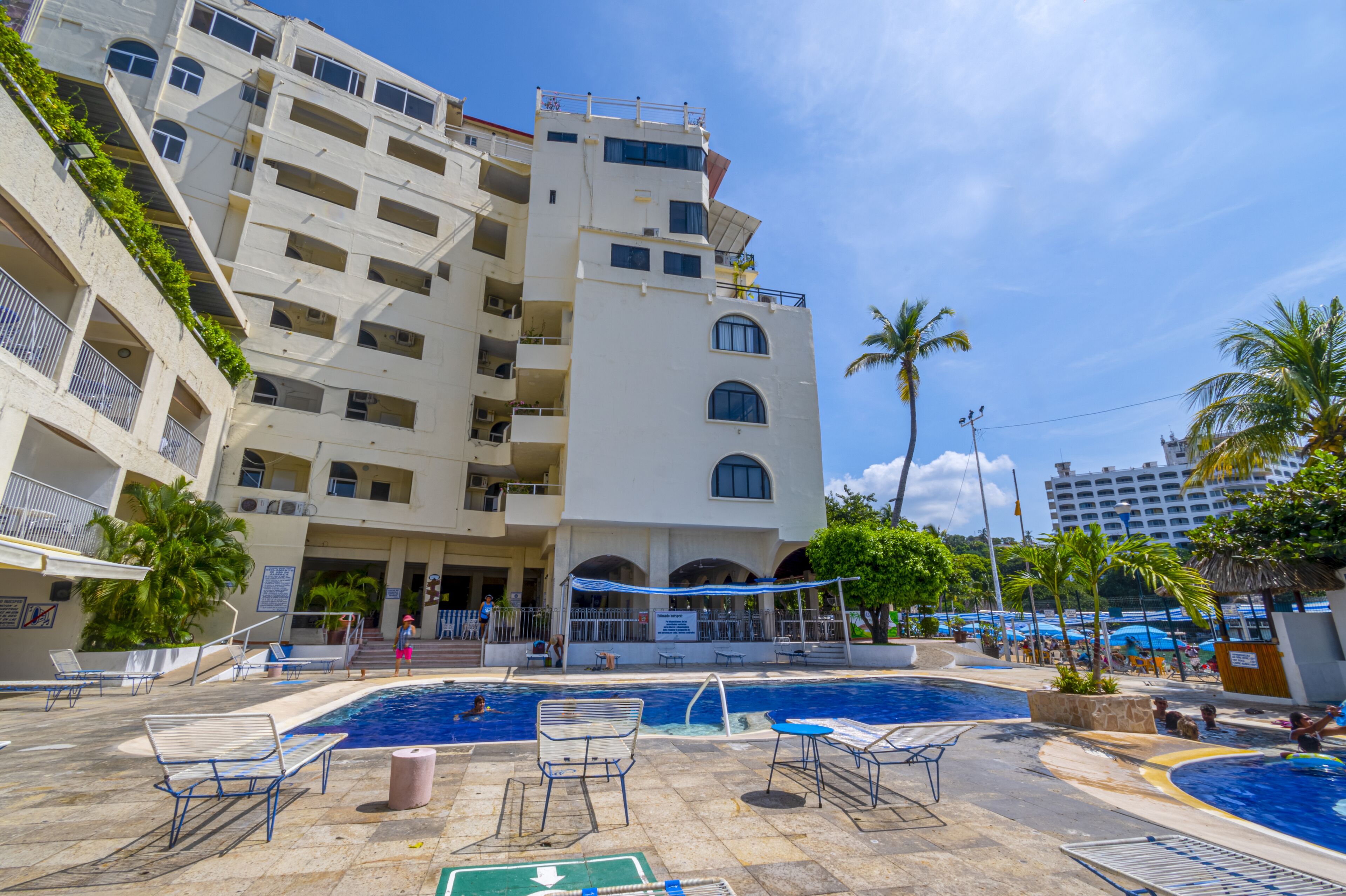 A hotel with a swimming pool, multiple balconies, and palm trees.