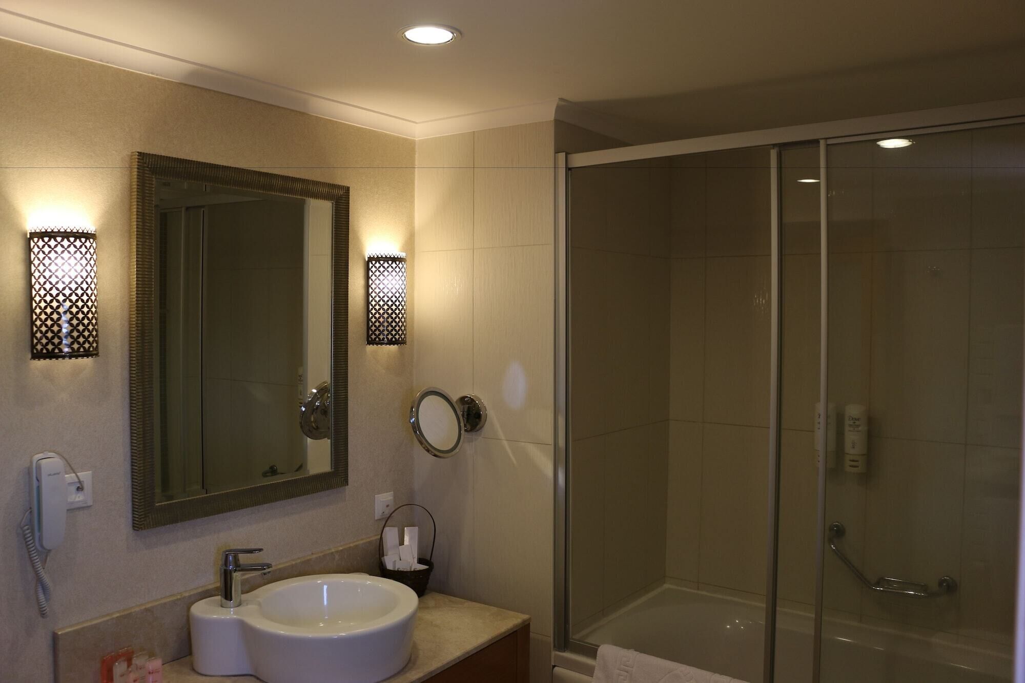 A bathroom with a large mirror, a sink, and a glass-enclosed shower.