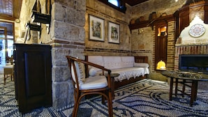 A stone-walled room with a wooden sofa, a chair, a table with glasses, and a fireplace. - Minyon Hotel (Antalya)