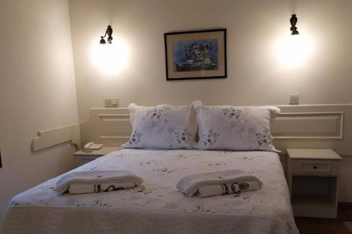 A neatly made bed with a white bedspread and pillows, two bedside tables with lamps, a framed picture on the wall, and a telephone on the nightstand.