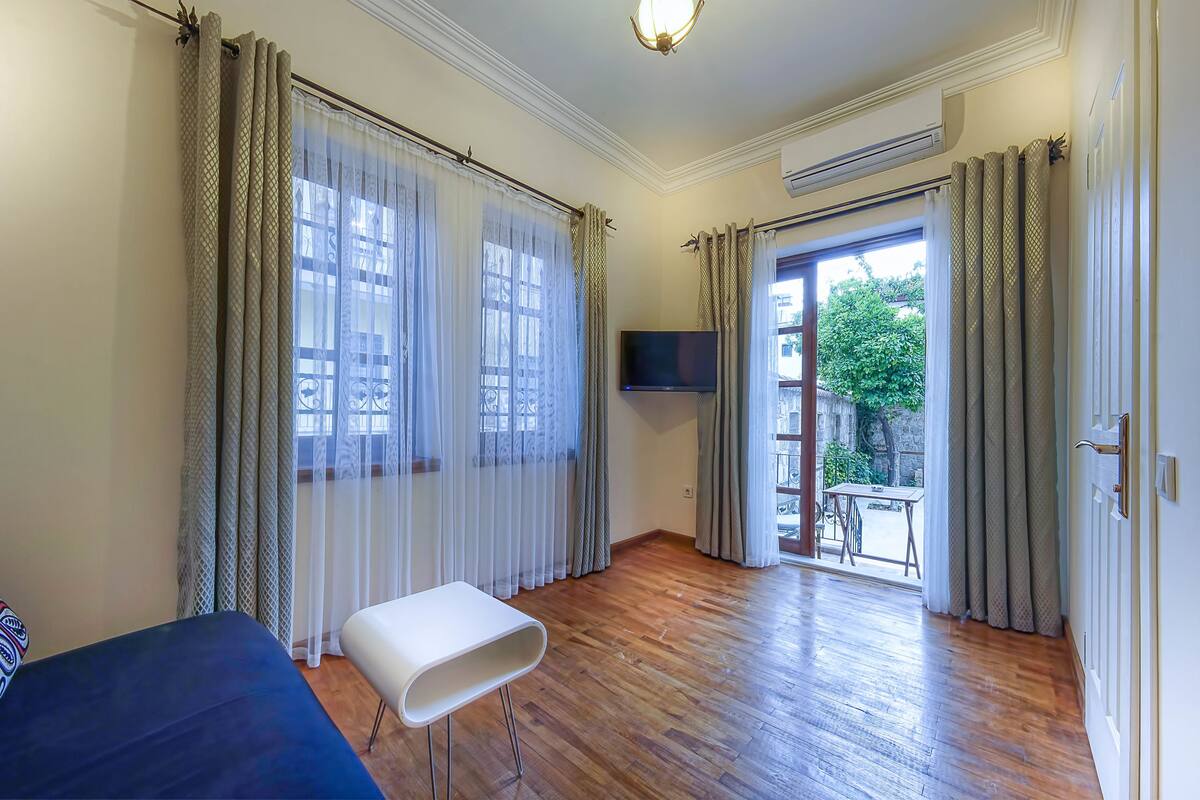 A hotel room with a bed, a small table, a TV, and a balcony with a view of the outside.