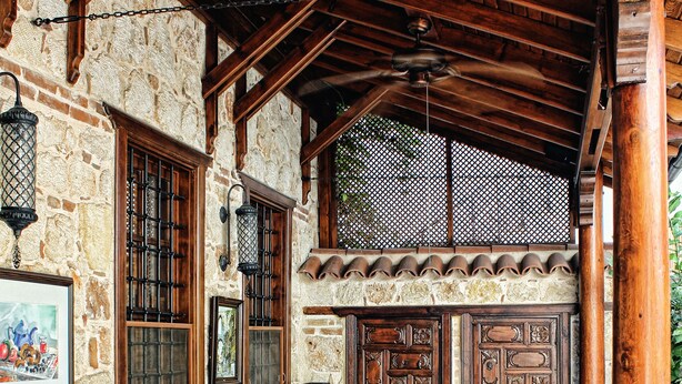 A rustic outdoor seating area with wooden tables and benches, stone walls, and a ceiling fan. - Minyon Hotel (Antalya)
