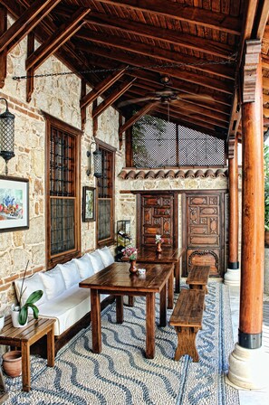 A rustic outdoor seating area with wooden tables and benches, stone walls, and a ceiling fan. - Minyon Hotel (Antalya)