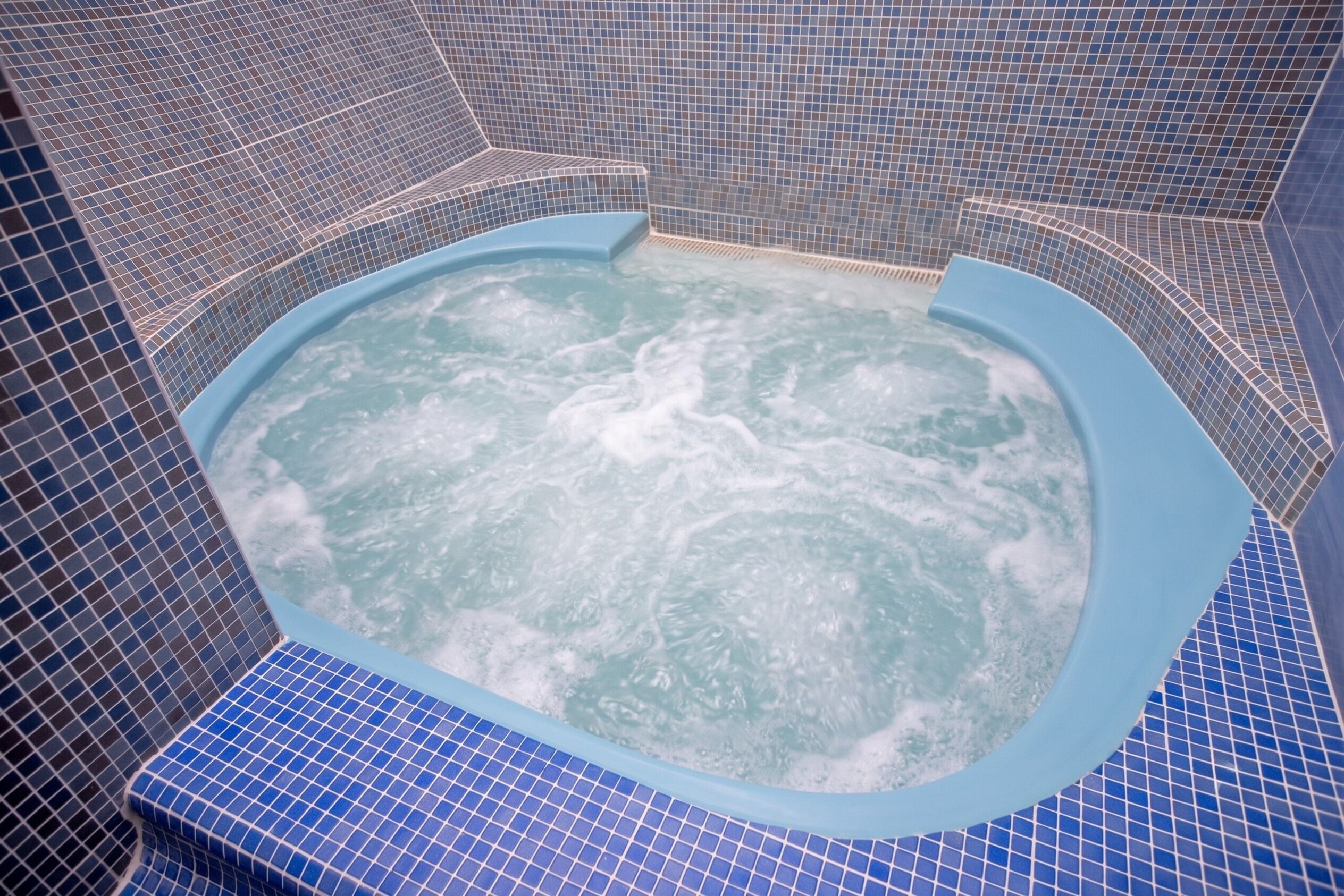 A hot tub with a blue tiled interior and a visible water jet feature.