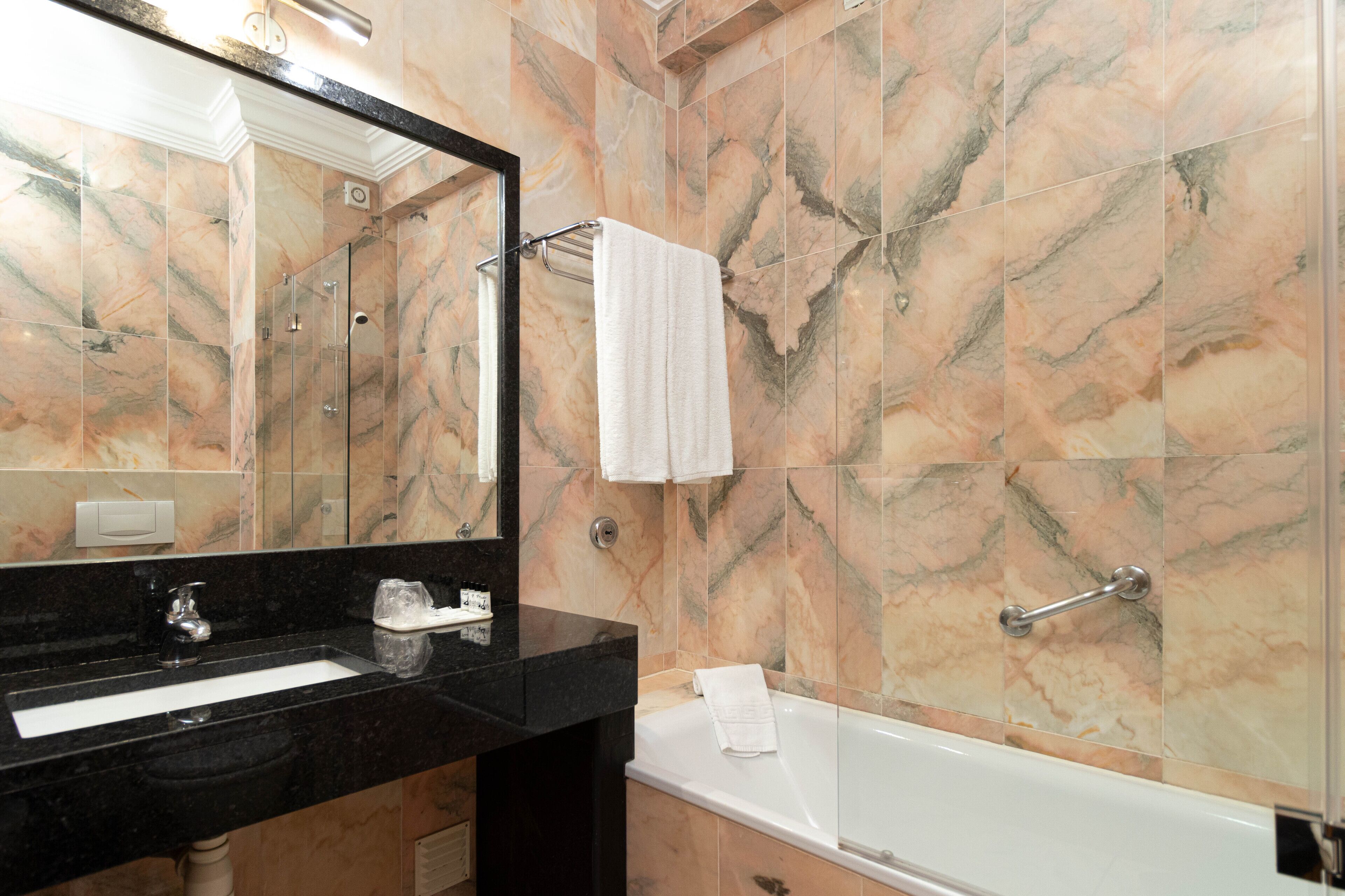 A bathroom with a black sink, a mirror, a white bathtub, and marble walls.