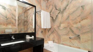 A bathroom with a black sink, a mirror, a white bathtub, and marble walls.