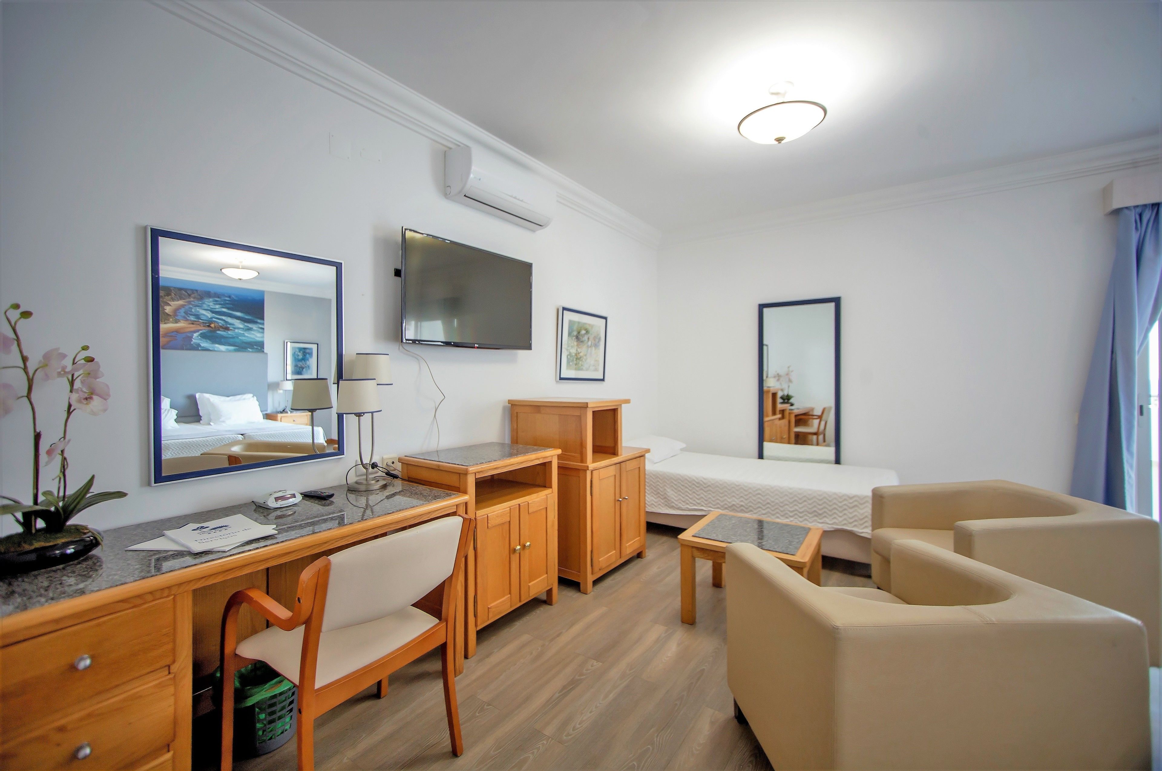 Una habitación de hotel con un escritorio de madera, una cama, un televisor y un espejo.