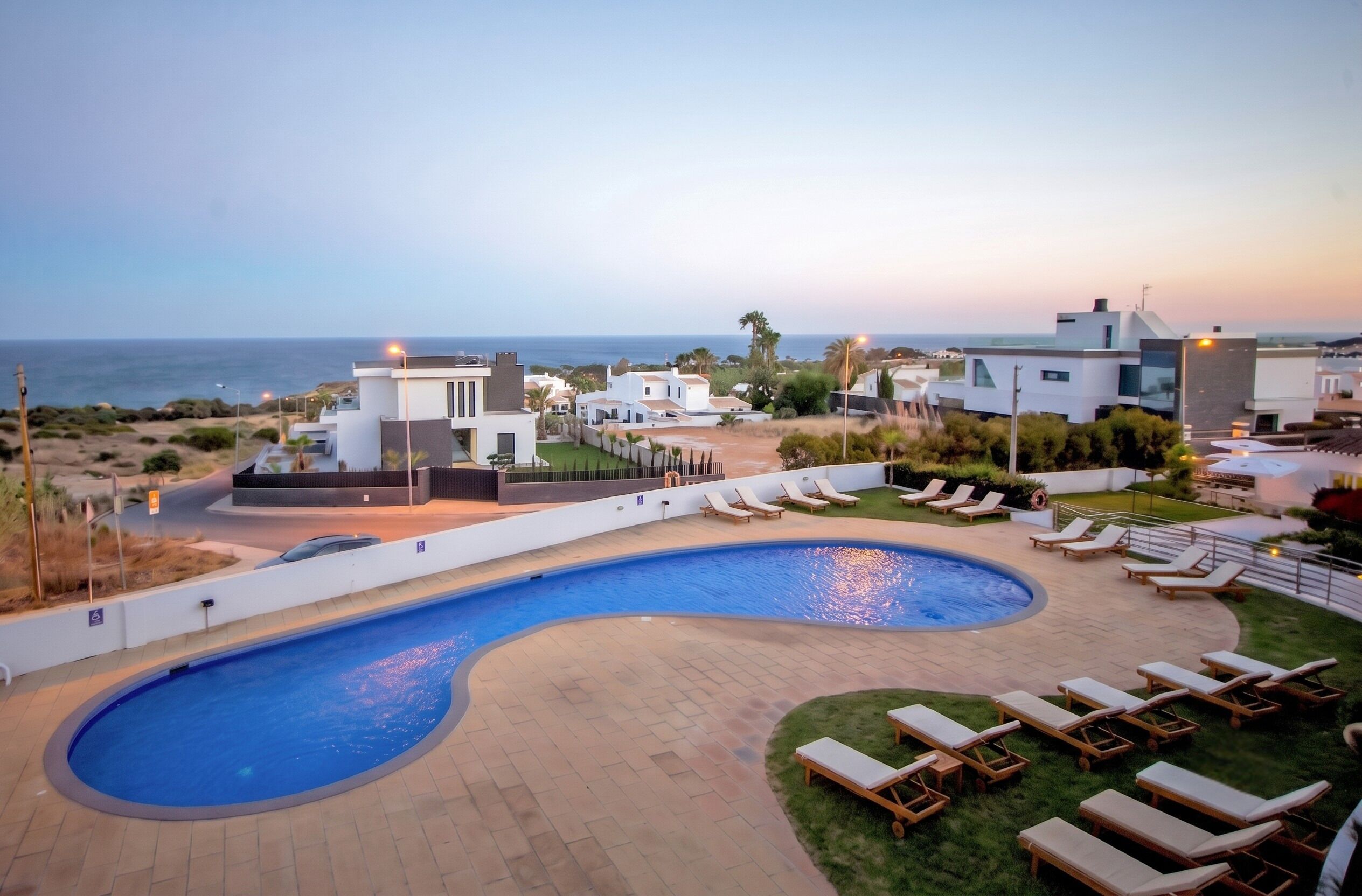 Una piscina con tumbonas, vistas al mar y edificios modernos.