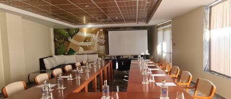 Un salón de conferencias con una larga mesa, sillas y una pantalla de proyector.