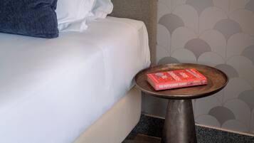 A bed with a white sheet and a pillow, a small round table with a book on it, and a wall with a scalloped pattern.