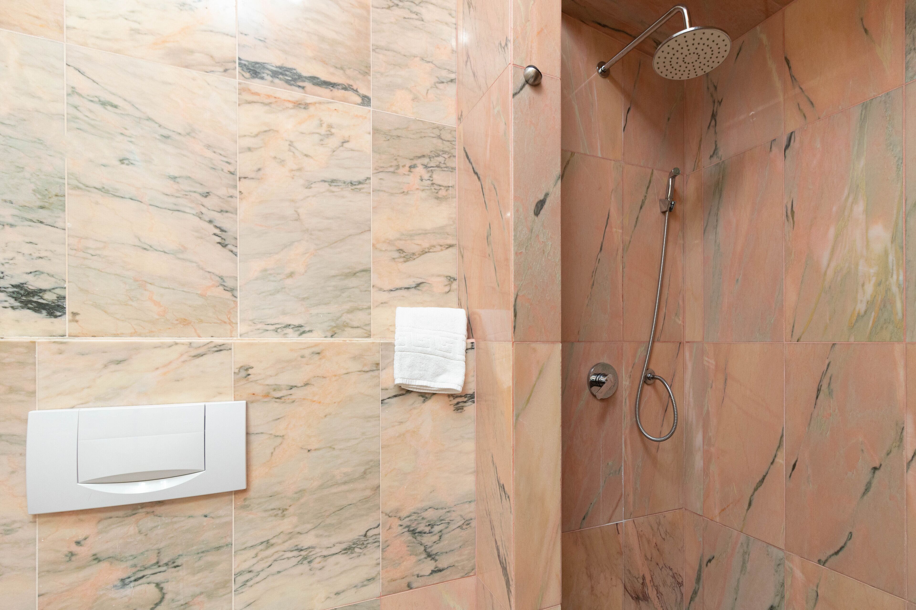 A bathroom with marble tiles, a shower with a handheld showerhead, and a towel dispenser.