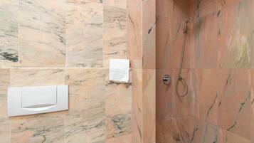 A bathroom with marble tiles, a shower with a handheld showerhead, and a towel dispenser.