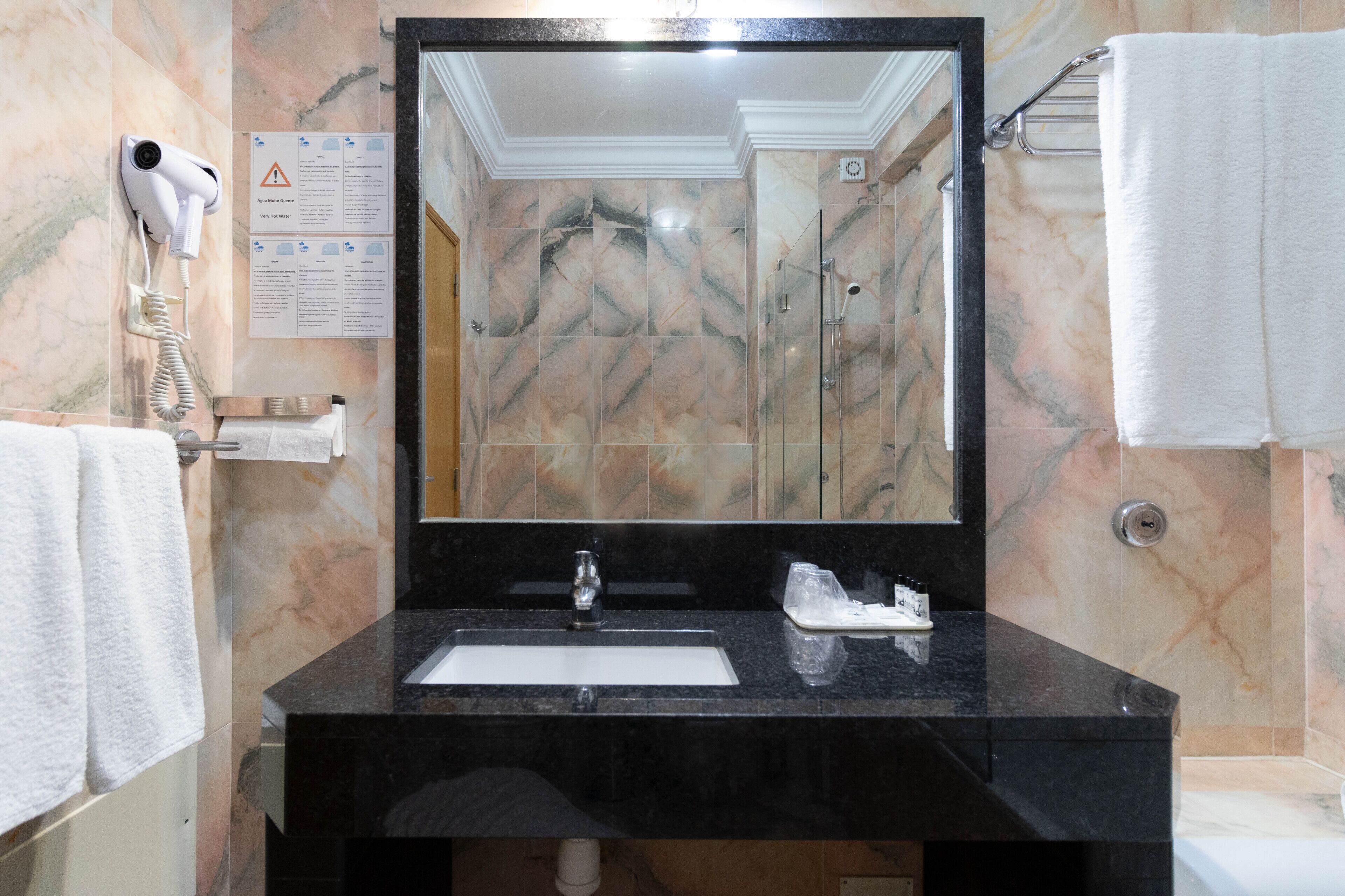 A bathroom with a black sink, a large mirror, a hair dryer mounted on the wall, and a shower area.