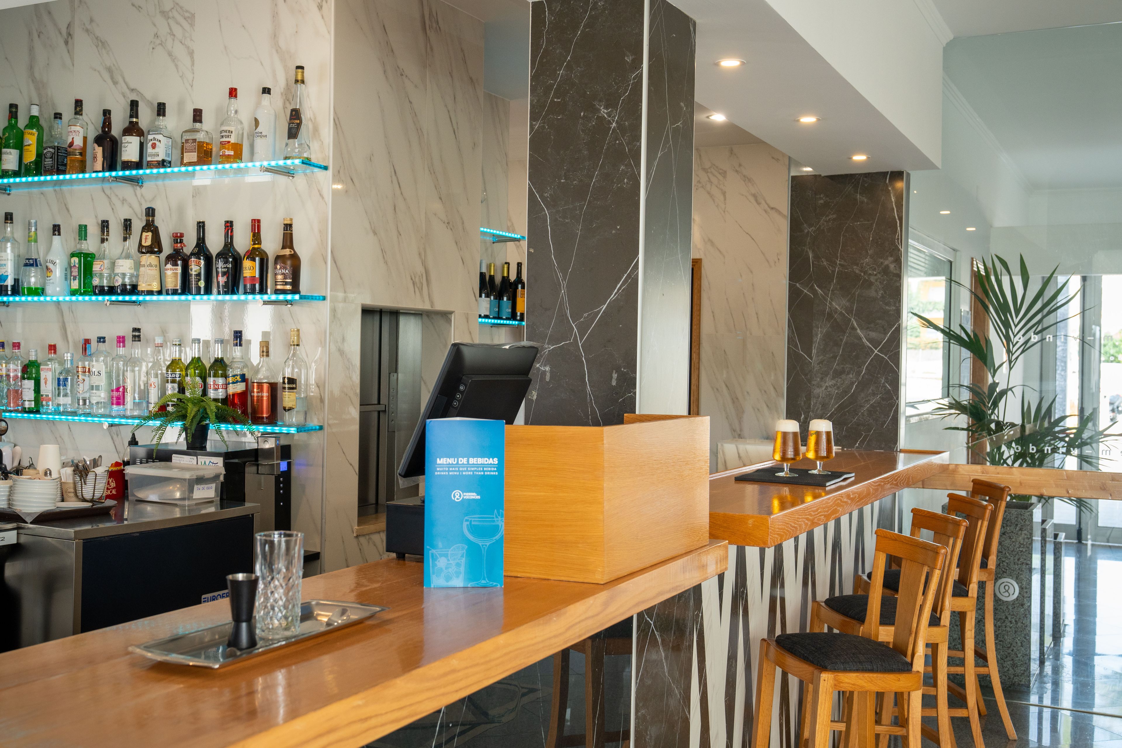 A bar area with a marble countertop, bar stools, and shelves with various liquor bottles.