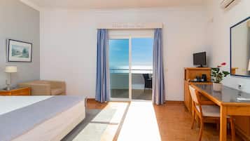 A hotel room with a bed, a desk with a computer, a TV, a potted plant, and a view of the outdoors.