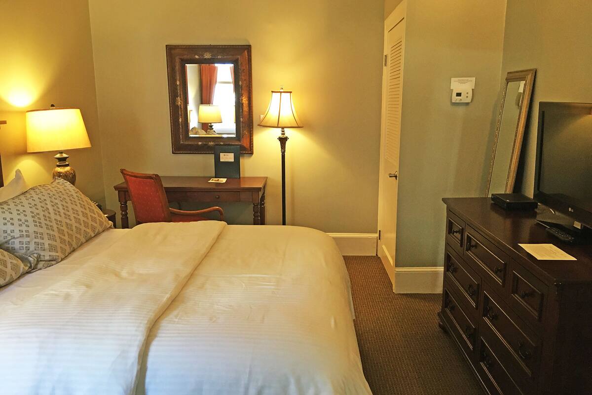 A hotel room with a bed, a desk, a chair, a dresser, and a television.