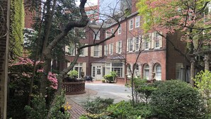 A brick building with a courtyard, surrounded by trees and shrubs.