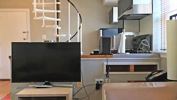 A living room with a television, a sofa, a kitchen area with appliances, and a staircase.