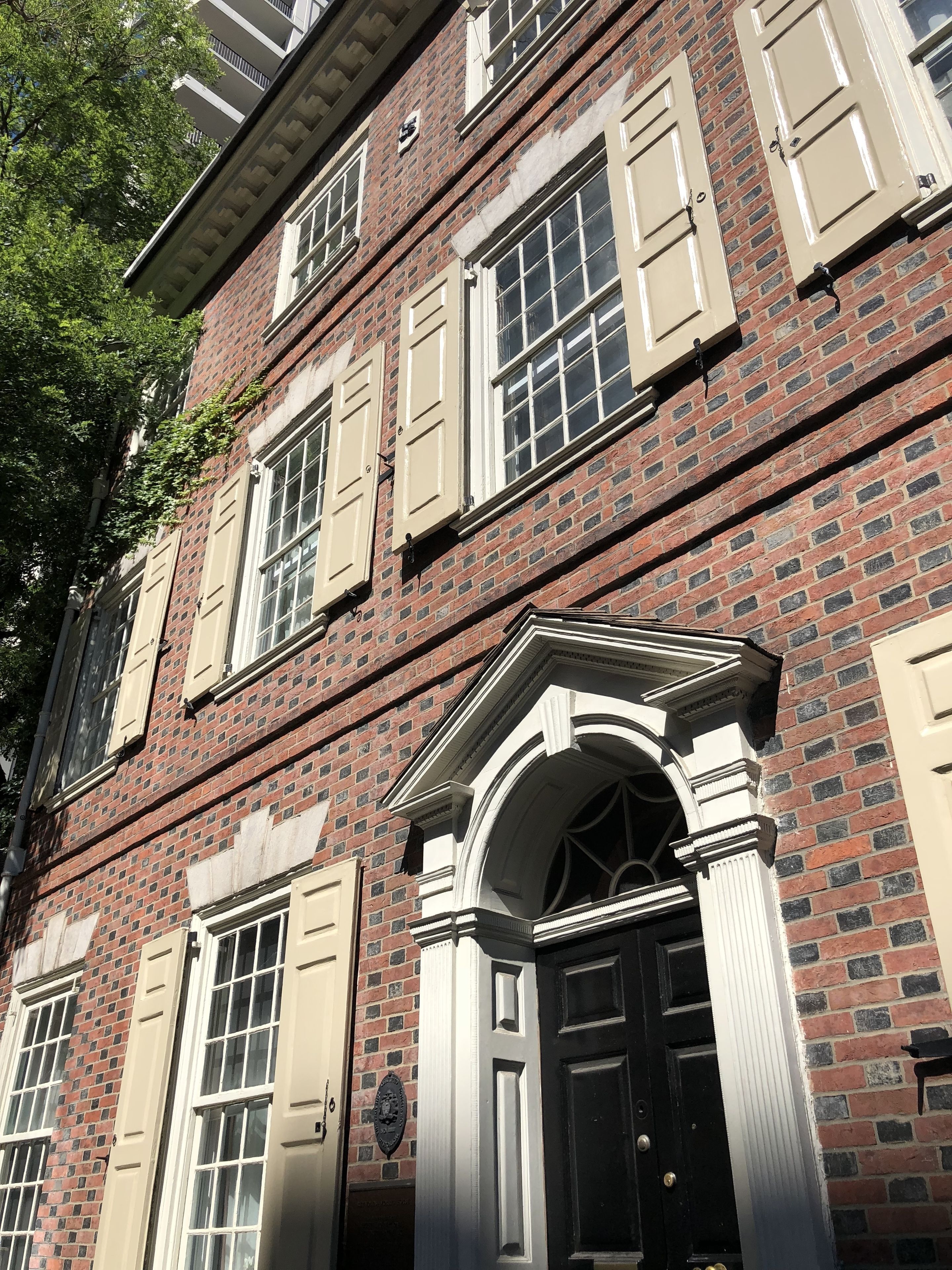 A multi-story brick building with beige shutters, a black door, and a classical architectural style.
