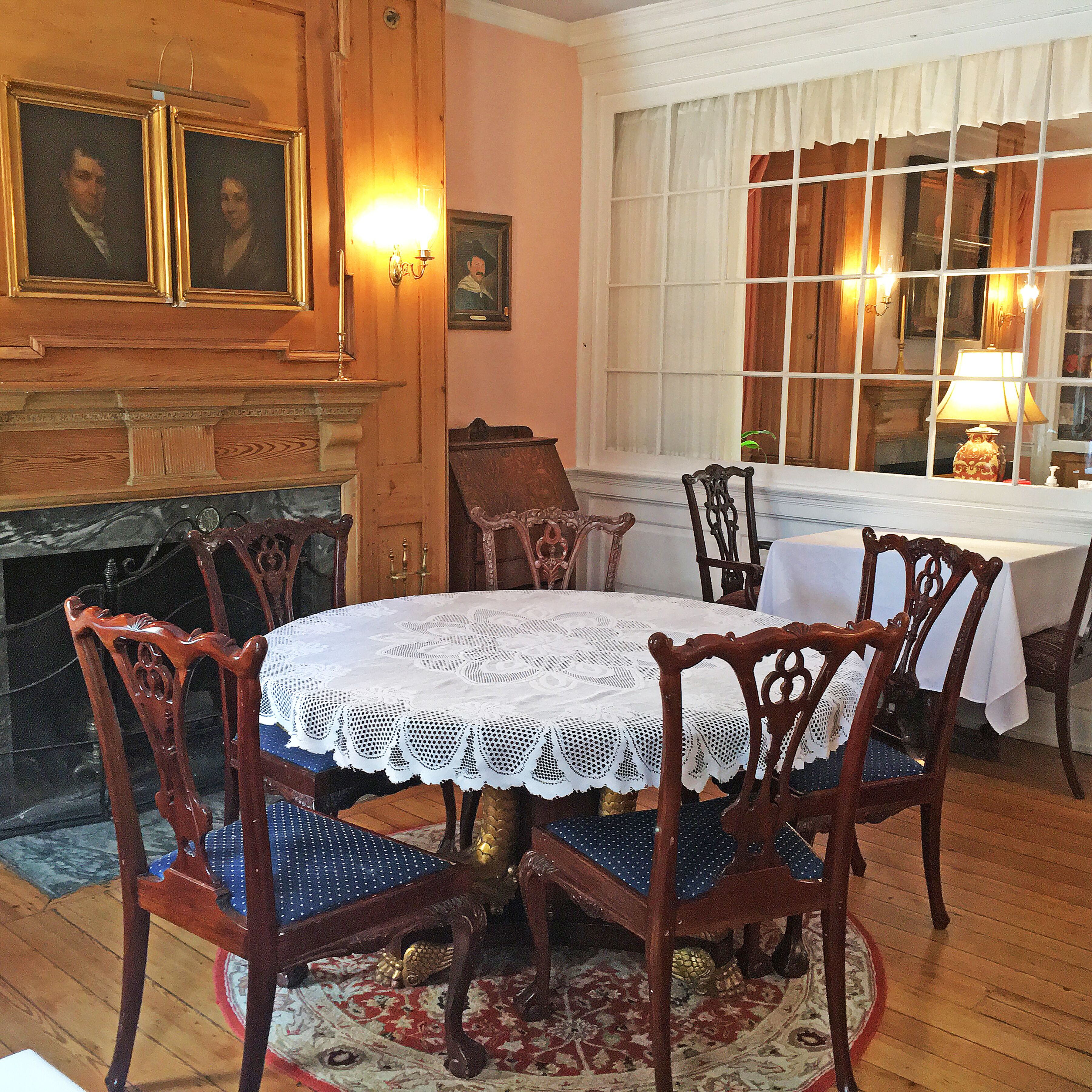 A dining room with a round table, chairs, a fireplace, and a window with curtains.
