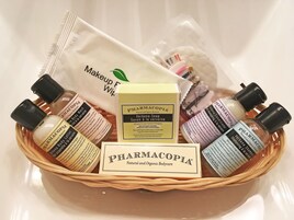 Cestino con diversi prodotti per la cura della pelle di PHARMACOPIA, tra cui lozione corpo, sapone e shampoo.