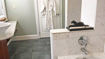 A bathroom with a bathtub, a sink, a mirror, a robe hanging on the door, and a statue on the countertop.