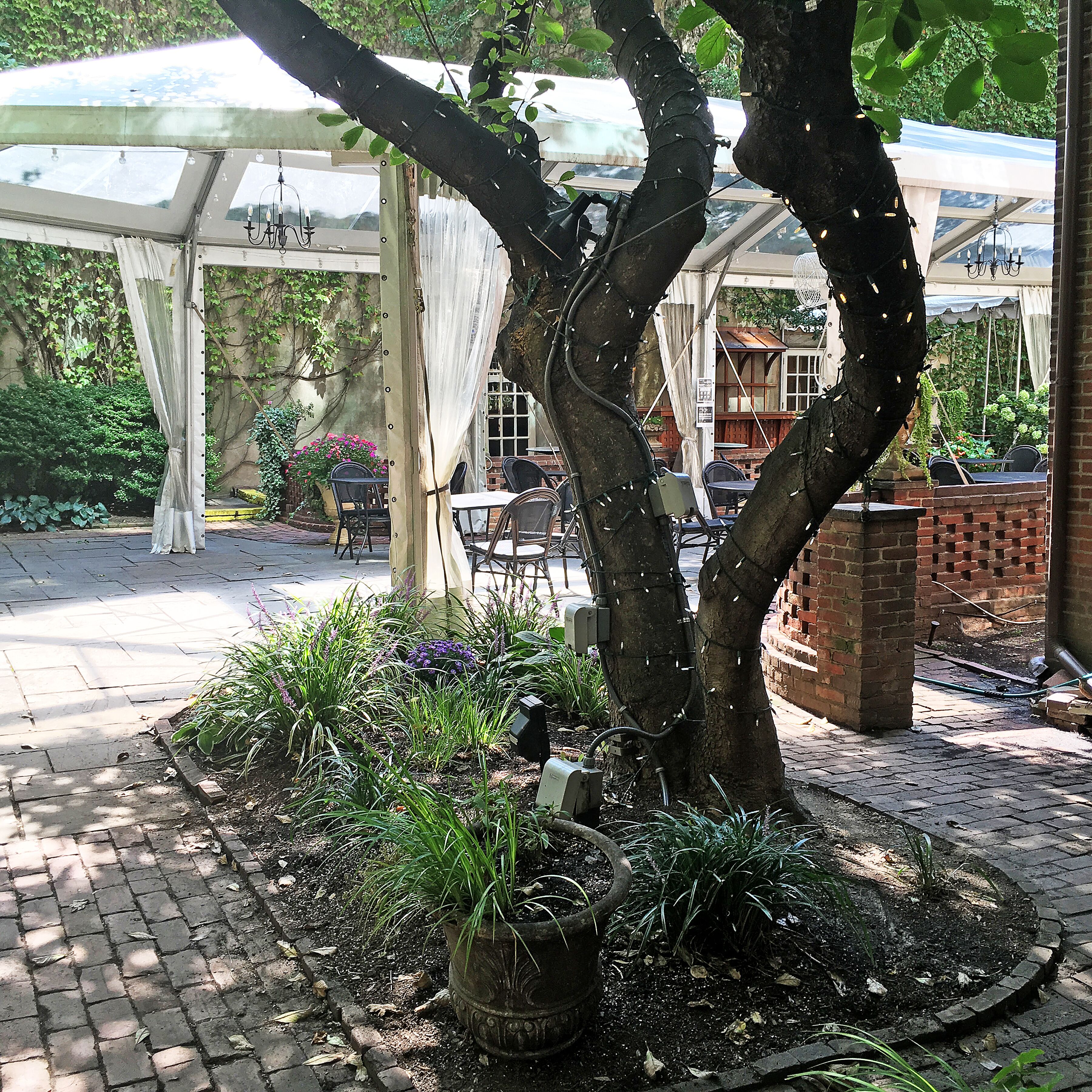 Un espacio al aire libre techado con pared de ladrillo, pérgola y jardín con diversas plantas.
