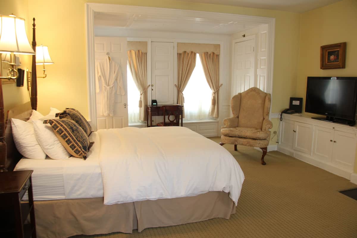 A hotel room with a large bed, a chair, a television, and a desk with a lamp.