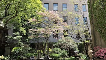 A courtyard with outdoor seating, surrounded by lush greenery and flowering trees.